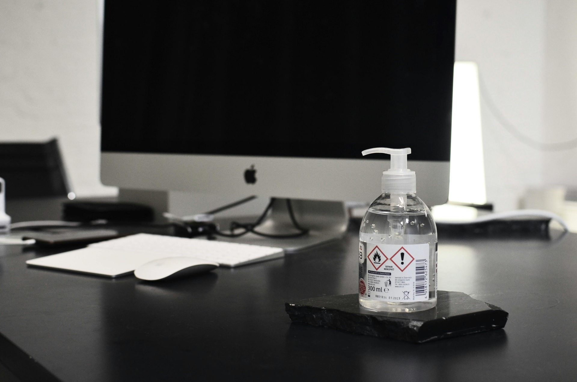 Flacon de gel antibactérien pour les mains posé sur une table, devant un moniteur moderne à écran noir, dans un espace de travail contemporain.